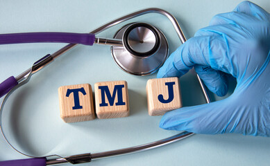 A hand in a medical glove puts cubes with the abbreviation TMJ on the background of a stethoscope