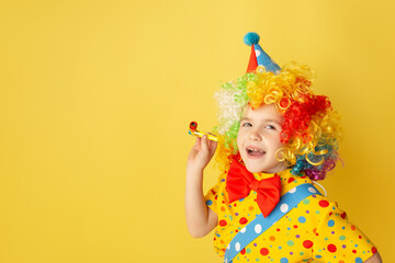 Funny kid clown against yellow background. Happy child playing with festive decor. Birthday and 1 April Fool's day concept