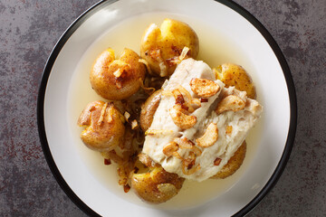 Traditional Bacalhau a Lagareiro Grilled Salted Cod with Olive Oil served with baked Potatoes closeup in the plate on the table. Horizontal top view from above