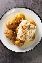 Traditional Portuguese Bacalhau a Lagareiro Oven Cooked Codfish with Potatoes closeup in the plate on the table. Vertical top view from above