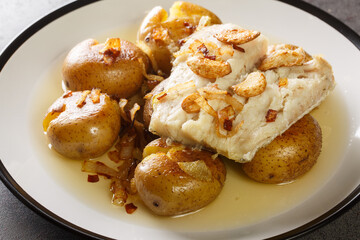 Cod fillet baked in olive oil with garlic served with potatoes close-up in a plate on the table....