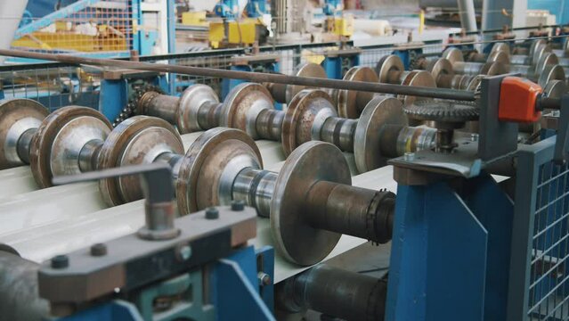 Close up metal sheet forming machine in metalwork factory. Steel rollers in metalforming machine for production roof tile in factory