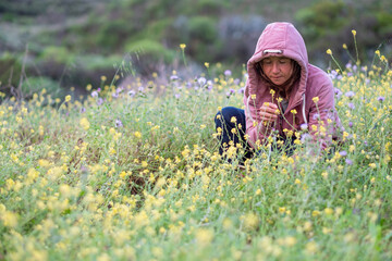 woman sitting in a meadow of yellow and purple flowers smelling the fragrance of flowers in springtime