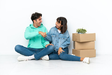 Young couple making a move while picking up a box full of things sitting on the floor isolated on white background handshaking after good deal