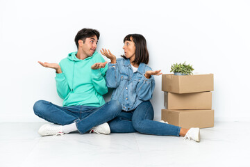 Young couple making a move while picking up a box full of things sitting on the floor isolated on white background making unimportant gesture while lifting the shoulders
