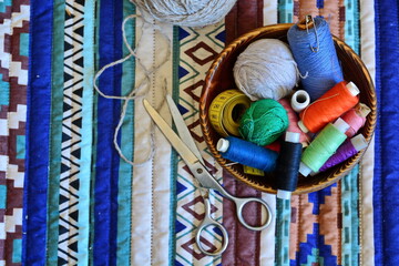 set for needlework and sewing – colorful threads, needles, yarn, scissors, measuring tape in a cup on a patterned background. top view, flat lay
