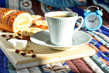 breakfast - cup of strong invigorating black coffee on background of fresh sweet pastries and coffee beans with sugar cubes on wooden board in bright morning sunlight and alarm clock on pattern cloth