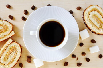 morning breakfast – white cup of strong invigorating black coffee on saucer between coffee beans with fresh sweet pastries and sugar on wooden board. top view, flat lay