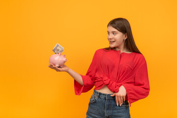 Young woman or girl holds piggy bank with money in hands and looks at it in surprise. Financial literacy concept.