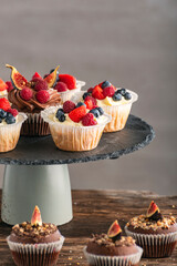 Muffin with berries on gray background. Chocolate and vanilla cupcakes with berry mix on the stand on wooden table. Vertical frame