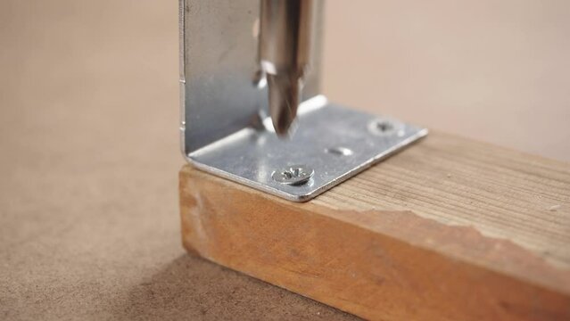Screwing L Shaped Brackets Corner Angles Metal Connector Hinge in wood with bolt. Close up view of craft working with cordless screwdriver and wooden door
