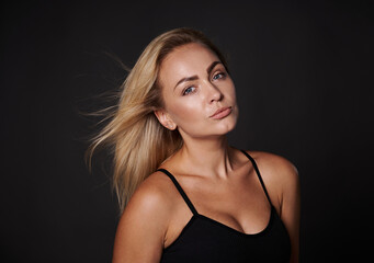 Beautiful attractive blonde body positive Caucasian woman in black bra posing against dark background with copy ad space. Confidence, self acceptance, healthy lifestyle. Love your body concept