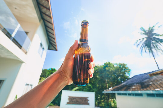 Vacation concept. Male hand holding bottle of beer against sunny sky.