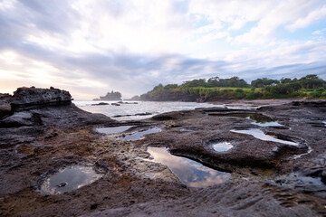 Beautiful balinese landscape. Ocean beach. Ancient hinduism temple Tanah lot on the rock against cloudy sky. Bali Island, Indonesia.