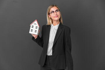 Blonde Uruguayan girl holding a house toy isolated on black background and looking up