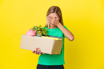 Young Uruguayan girl making a move while picking up a box full of things isolated on yellow background with tired and sick expression
