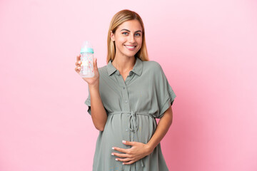 Young Uruguayan woman isolated on blue background pregnant and holding a feeding bottle