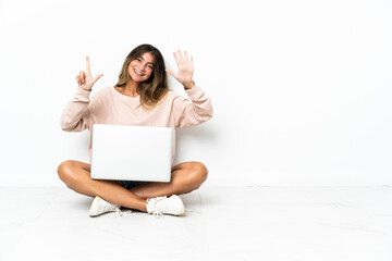 Young woman with a laptop sitting on the floor isolated on white background counting seven with fingers