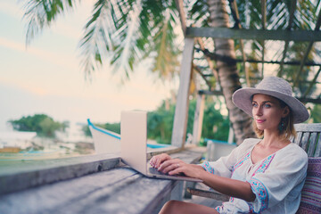 Technology and travel. Working outdoors. Freelance concept. Pretty young woman using laptop in cafe on tropical beach.