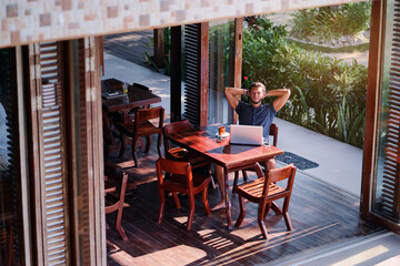 Freelance concept. Relaxed young bearded man working on laptop computer while sitting on terrace.