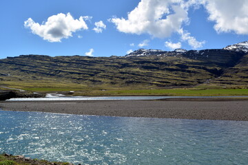 Fototapeta na wymiar River against the backdrop of snow-capped peaks of the mountains of basalt in the eastern fjords of Iceland