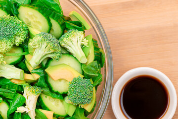Fresh Green Salad of Avocado, Broccoli, Spinach and Cucumber for Detox with Soy Sauce on Wooden Cutting Board. Vegan Salad. Vegetarian Culture. Raw Food. Healthy Eating and Vegetable Diet