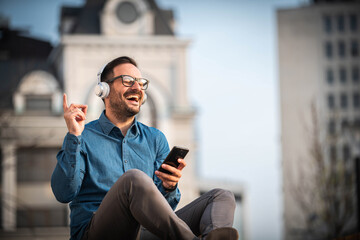 Young male model listening music using wireless headphones, after he finished his job. Enjoying in music, singing.