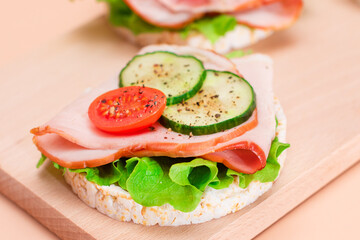 Light Breakfast. Quick and Healthy Sandwiches. Rice Cakes with Ham, Tomato, Fresh Cucumber and Green Salad on Wooden Cutting Board. Beige Background