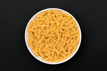 Uncooked Fusilli Pasta Lying on White Plate on Black Background. Raw and Dry Macaroni. Unhealthy and Fat Food - Top View