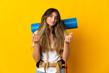 Young mountaineer woman with a big backpack isolated on yellow background making money gesture