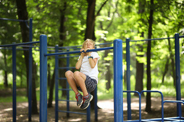 Obraz premium the boy athlete in the park pulls himself up on the horizontal bar grimaced and pulls himself up with effort