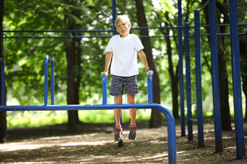 athlete boy in the park hung on his hands and does exercises on the uneven bars