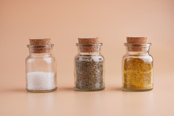Three glass jars with cork lids containing spices: coarse sea salt, oregano, curry on yellow seamless surface