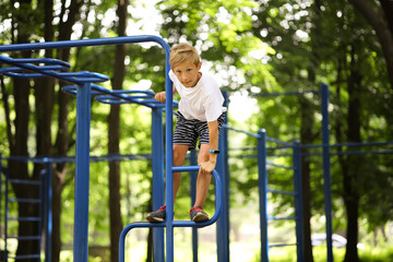 Obraz premium the boy athlete is in the park on the sports ground climbed on the horizontal bars and try to play sports