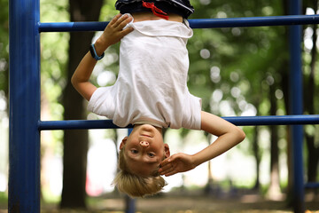 the boy athlete on the sports ground in the park caught his feet on the stairs and hangs upside...