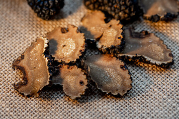 Fototapeta na wymiar Truffles on a beige burlap. Thinly sliced mushrooms. Black raw champignons on the surface. Top view. Dark blurred background. The artistic intend and the filters. Subject is out of focus.
