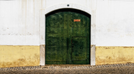 green metal door with a white and yellow house front on a cobblestone street
