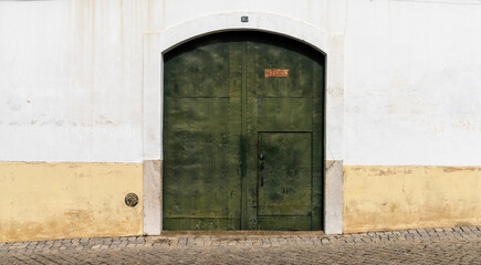 green metal door with a white and yellow house front on a cobblestone street