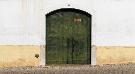 Fototapeta premium green metal door with a white and yellow house front on a cobblestone street