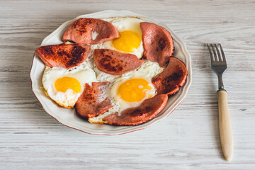 Fried eggs with sausage on a plate on a wooden table