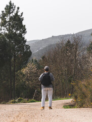 Rear view of a girl with backpack and hat walking alone on a dirt road