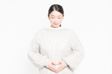 白い背景の前に立ってお腹に手を当てている女性