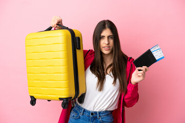 Young caucasian woman isolated on pink background unhappy in vacation with suitcase and passport