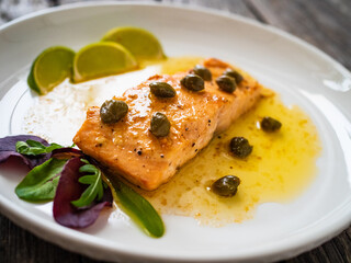 Butter sauce fried salmon steak with capers and lime  on wooden table
