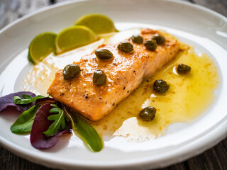 Butter sauce fried salmon steak with capers and lime  on wooden table
