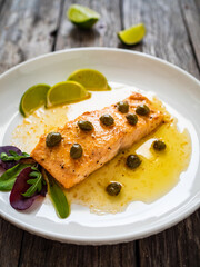 Butter sauce fried salmon steak with capers and lime  on wooden table
