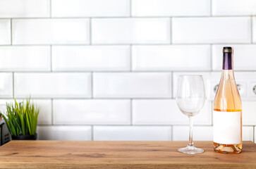 Wooden table on blurred background of kitchen space with white tile brick wall with bottle of rose wine and wineglass