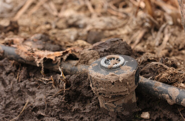 Sprinkler in the mud against the background of brown plants after the snow melts in spring