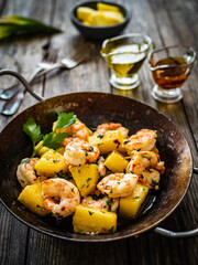 Fried prawns and pineapple in frying pan on wooden table
