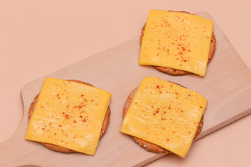 Crispy Cracker Sandwiches with Cheese and Paprika on Wooden Cutting Board and Beige Background